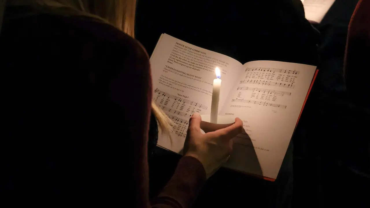 Over the shoulder of a worshipper holding a lit candle above an open service booklet at the Silent Night candlelighting on Christmas Eve
