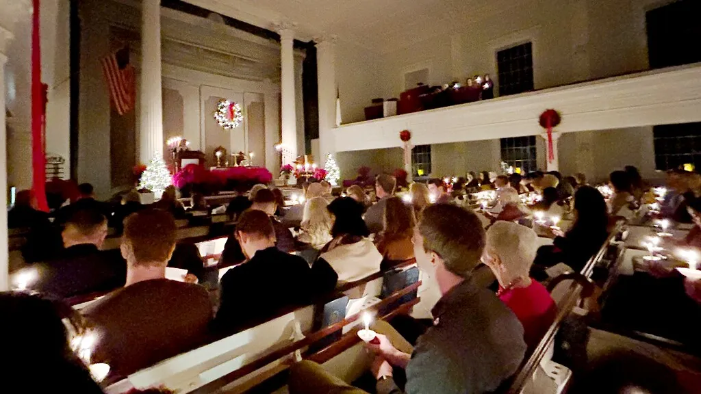 A congregation holding lit candles in the pews of a church decorated for Christmas, during a Christmas Eve candlelight service