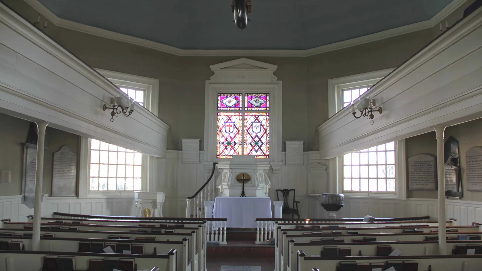 The white-paneled sanctuary of Gloria Dei (Old Swedes') Church, with box pews, side balconies and a stained glass window above the altar