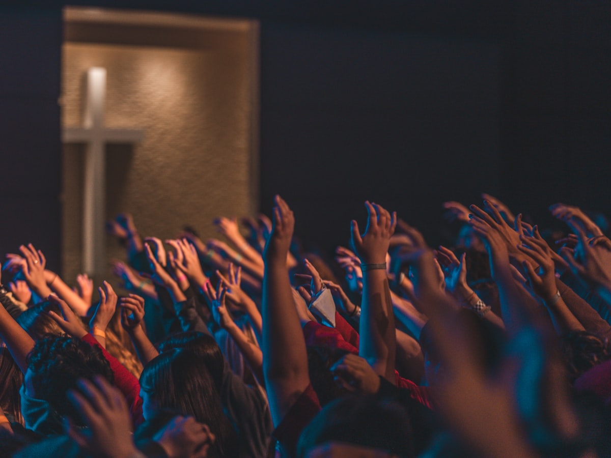 Church worship crowd with hands raised and cross in background
